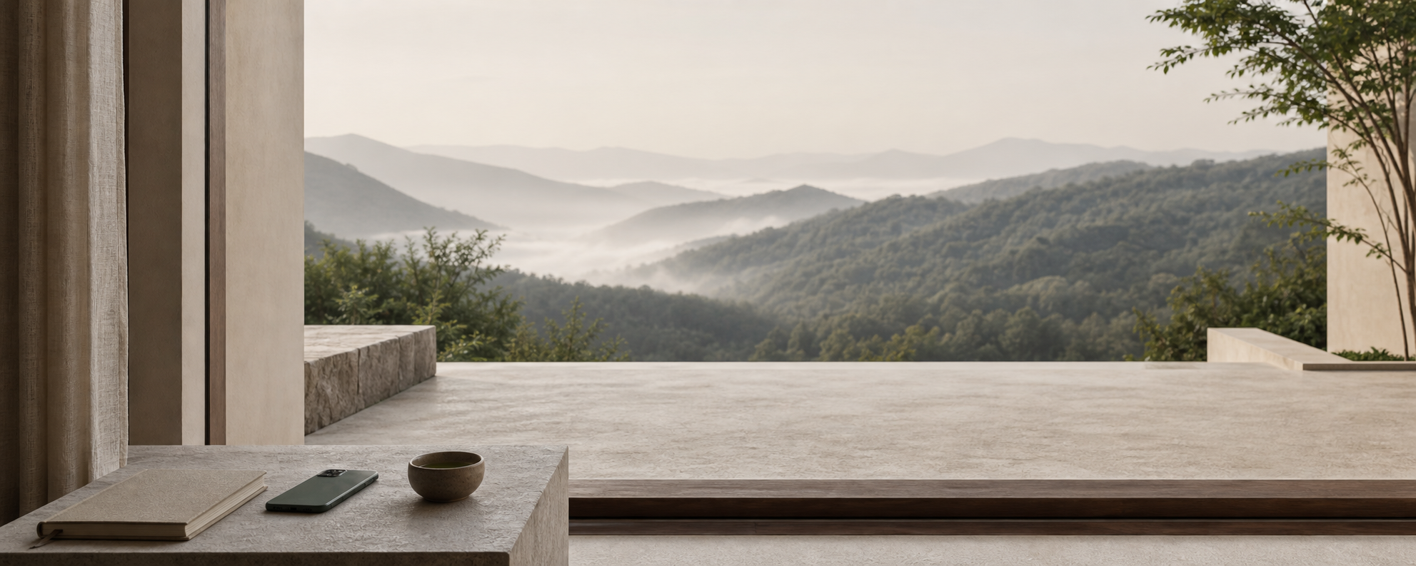 A quiet mountain home terrace with a notebook, phone, tea, and misty forested hills